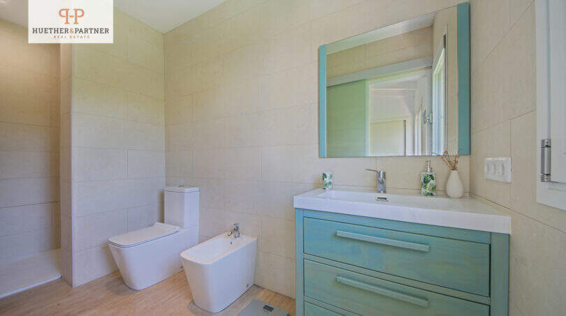 Helles Badezimmer mit türkisem Waschtischunterschrank, Bidet, WC und Holzboden im Einfamilienhaus Sa Ràpita.