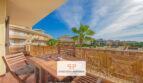 Sonnige Dachterrasse mit Holzmöbeln, Bambuseinfassung und Blick auf Palmen und umliegende Häuser in Cales de Mallorca.
