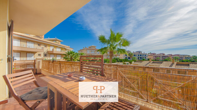 Sonnige Dachterrasse mit Holzmöbeln, Bambuseinfassung und Blick auf Palmen und umliegende Häuser in Cales de Mallorca.