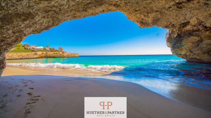 Blick aus einer Meereshöhle auf türkisblaues Wasser und Sandstrand in Cales de Mallorca