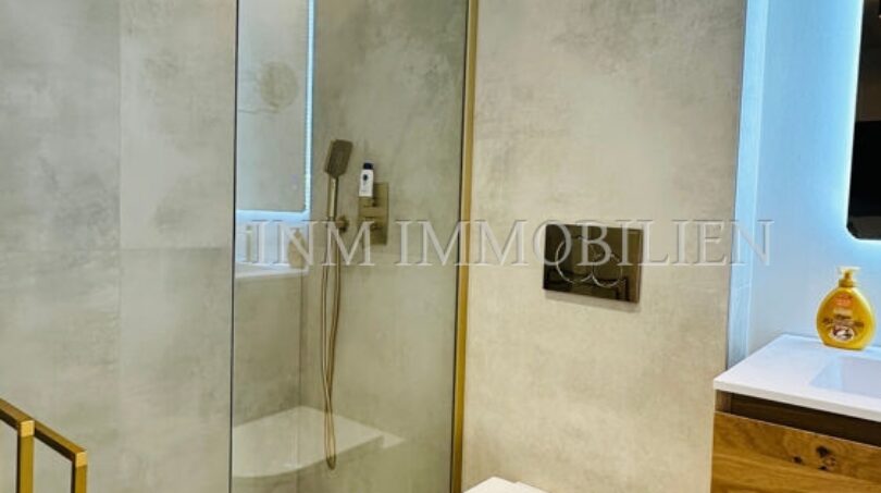 Modern designer bathroom with walk-in shower, gold accents and wall-hung toilet in Mallorca luxury apartment.