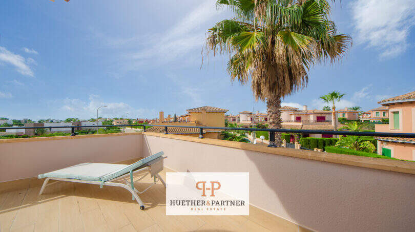 Sonnige Dachterrasse mit Liegestuhl, Palme und Blick auf die Villen von Cala Murada unter blauem Himmel.