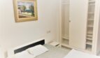 Helles Schlafzimmer der Ferienwohnung Cala Ratjada mit Doppelbett, weißem Einbauschrank und Landschaftsgemälde