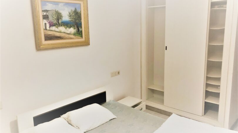 Helles Schlafzimmer der Ferienwohnung Cala Ratjada mit Doppelbett, weißem Einbauschrank und Landschaftsgemälde
