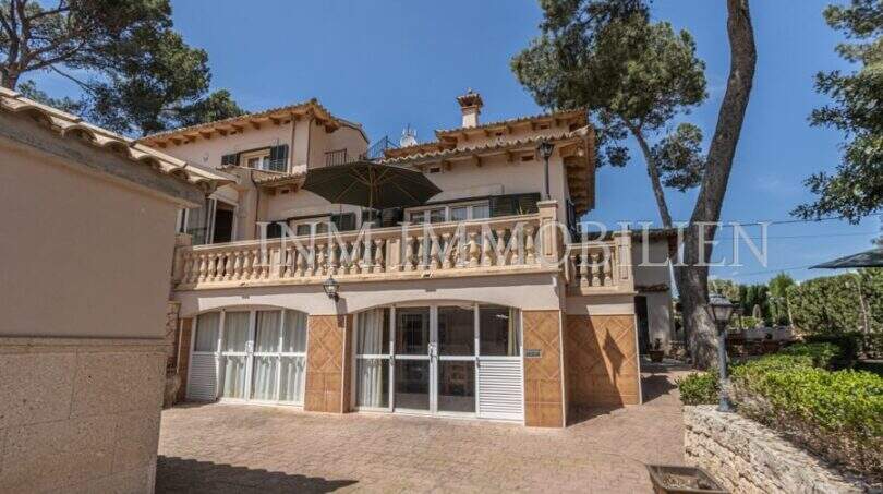 Außenansicht der Villa in Marratxí mit Terrasse, Balkon, Sonnenschirm und gepflastertem Innenhof, umgeben von Pinien.