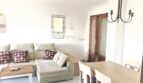 Helles Wohnzimmer der Mietwohnung in Cala Ratjada mit Ecksofa, Esstisch und elegantem Kronleuchter.