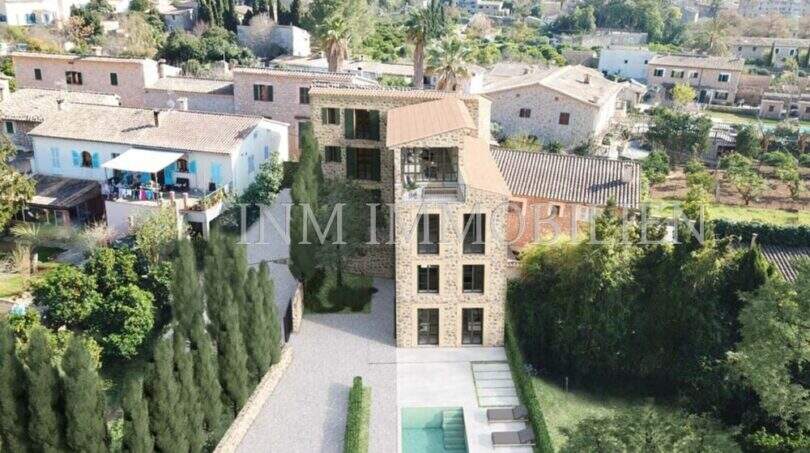 Vista aérea de una finca de piedra natural en Sóller con piscina, jardín y edificios de pueblo circundantes.