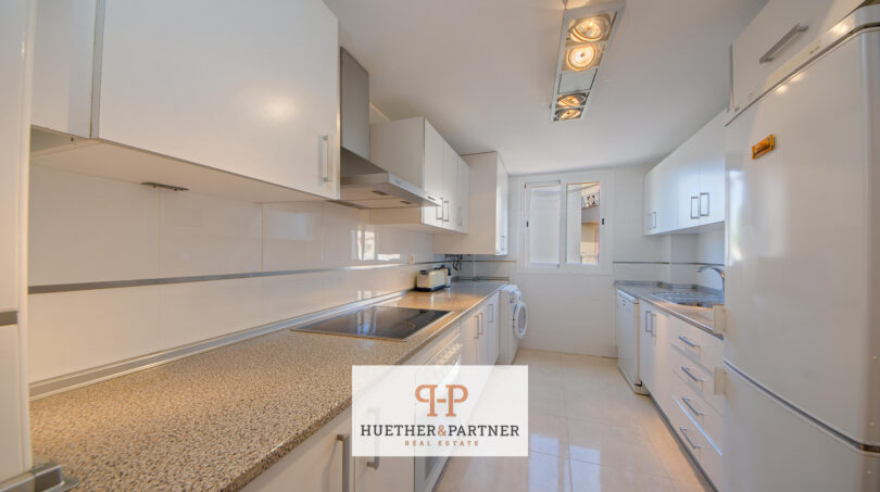 Helle, moderne Küche der Mallorca-Wohnung mit weißen Schränken, Granitarbeitsplatte und Einbaugeräten.