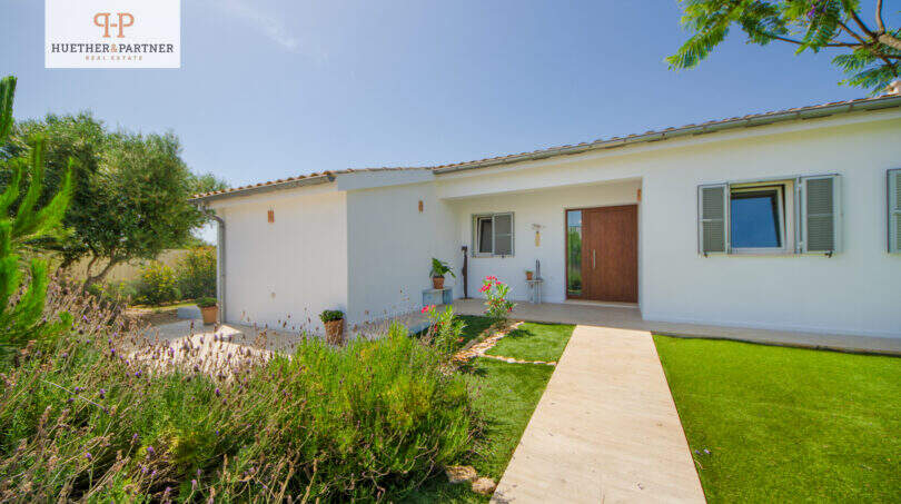 Außenansicht Einfamilienhaus Sa Ràpita: weißes Gebäude, gepflegter Rasen, Holzweg, Lavendelbepflanzung, mediterraner Garten.