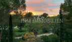 Puesta de sol sobre jardín cuidado con villa mediterránea en Bendinat, vista desde la terraza del ático