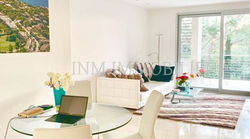 Salón luminoso con mesa de cristal de comedor, sillas blancas, sofá y acceso a la terraza en moderno ático Bendinat