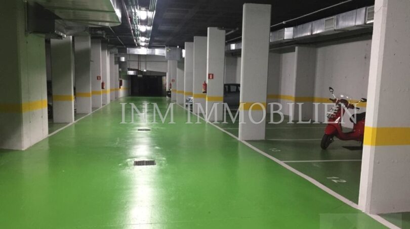 Garaje subterráneo del ático en Bendinat con suelo verde, plazas de aparcamiento y scooter rojo