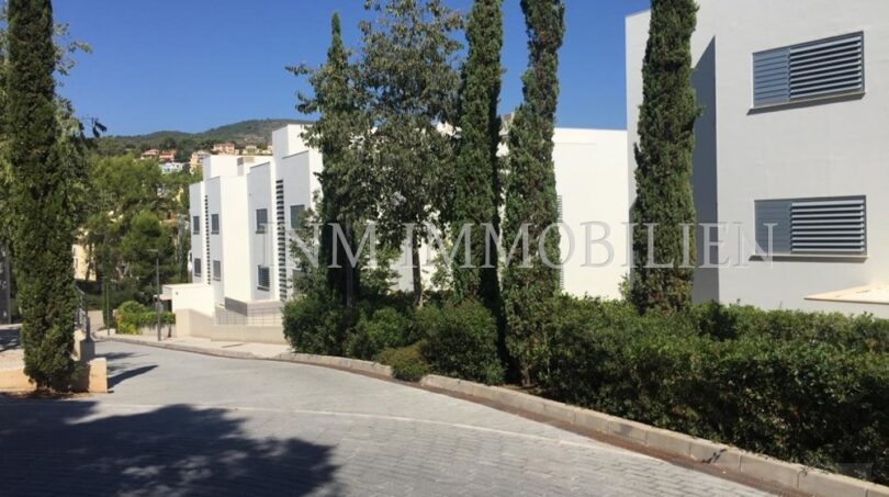 Vista exterior de casas adosadas modernas en Bendinat con verde cuidado, cipreses y acceso curvo.