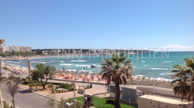 Panoramablick vom Balkon auf den belebten Strand von El Arenal mit türkisblauem Meer und Palmen.