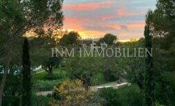Garden area with Mediterranean vegetation and view of penthouse complex in Bendinat at sunset.