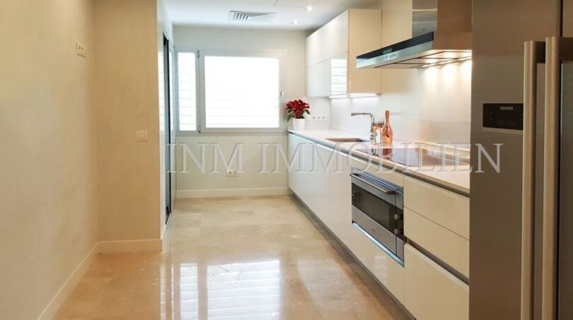 Modern fitted kitchen with white high-gloss fronts, Siemens appliances and marble floor in penthouse Bendinat