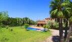 Finca Campos: spacious garden with pool, palms and Mediterranean country house under blue sky.
