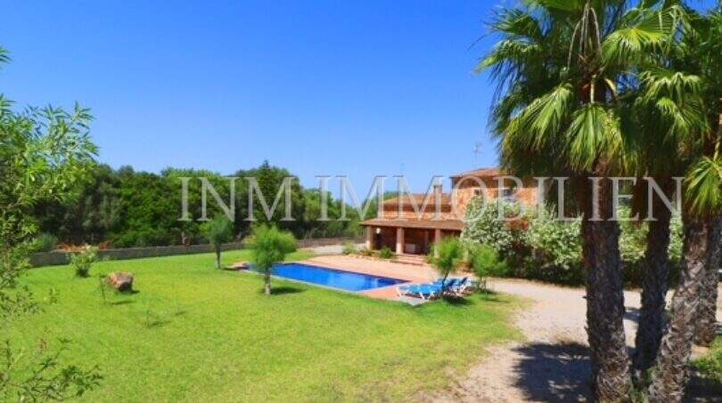 Finca Campos: spacious garden with pool, palms and Mediterranean country house under blue sky.
