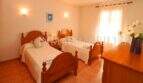 Bright bedroom of the finca near Campos with two wooden beds, terracotta floor and window with curtains.