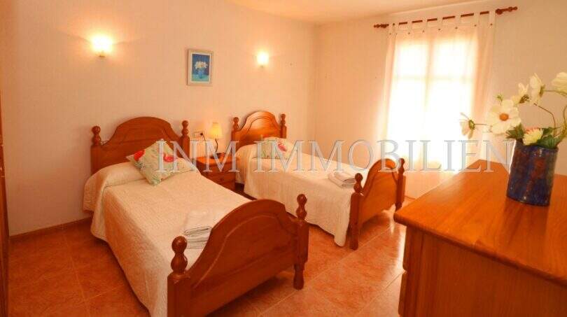 Bright bedroom of the finca near Campos with two wooden beds, terracotta floor and window with curtains.