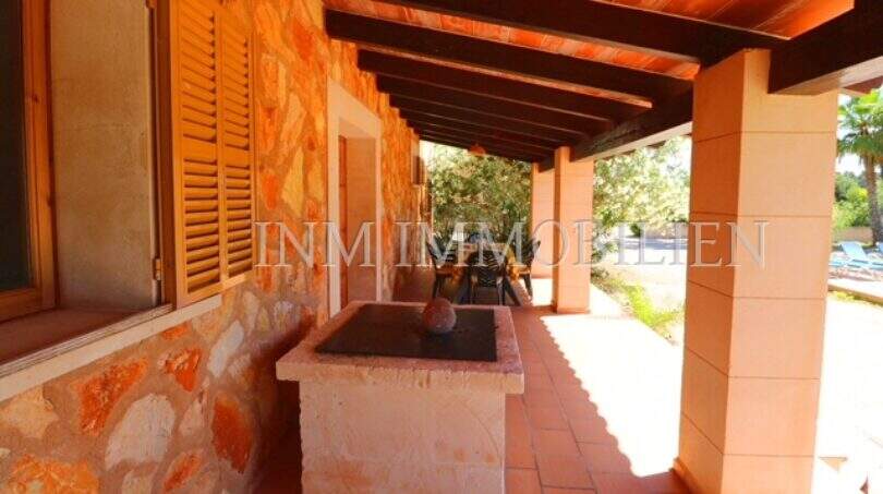 Covered terrace of the finca near Campos with barbecue station, wooden ceiling and natural stone wall.
