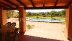 Covered terrace with dining table of the finca near Campos, view of swimming pool and green garden area.