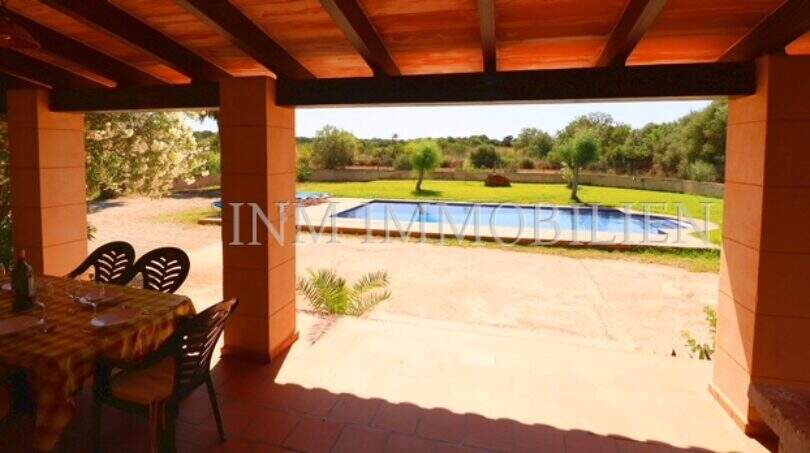 Covered terrace with dining table of the finca near Campos, view of swimming pool and green garden area.