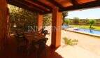 Covered terrace with dining table of the finca near Campos, view of pool and green garden area.