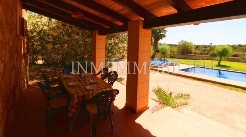 Covered terrace with dining table of the finca near Campos, view of pool and green garden area.