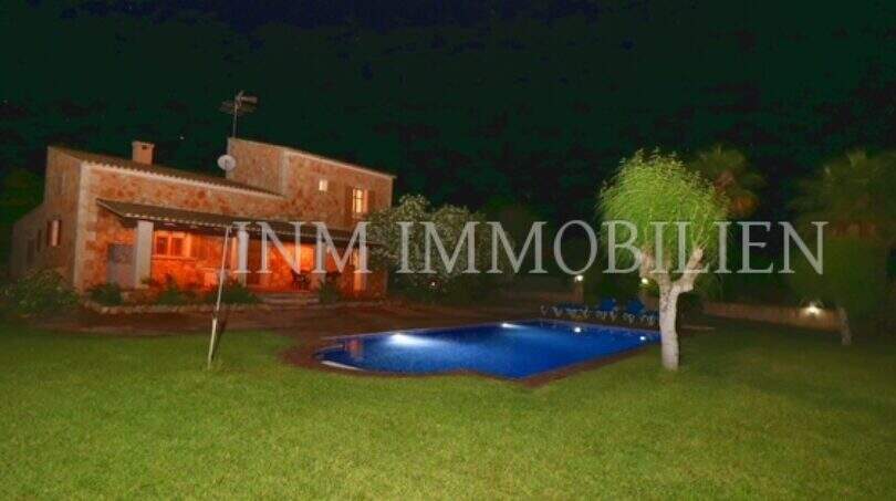 Finca Campos at night: illuminated pool, well-maintained lawn and rustic stone house with warm lighting.