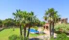 Spacious garden of the finca near Campos with pool, palms and green lawn under blue sky.