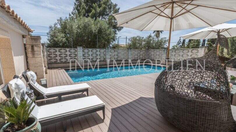 Sonnige Poolterrasse mit Holzdeck, Liegestühlen und Rattansessel der Villa in Marratxí