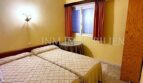 Helles Schlafzimmer mit zwei Einzelbetten, gelben Wänden und roten Vorhängen in Meereslinie-Wohnung El Arenal
