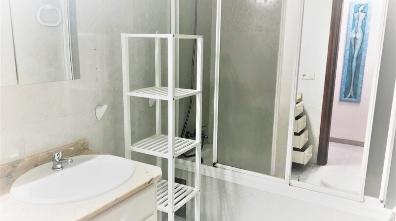 Helles Badezimmer der Ferienwohnung in Cala Ratjada mit Duschkabine, Waschbecken und weißem Regal.