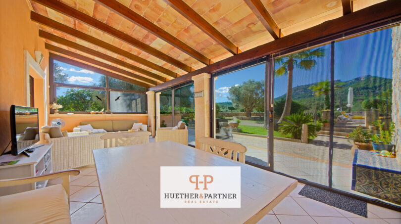 Terraza cubierta de la finca Felanitx con techo de vigas de madera, mesa de comedor y vistas a la piscina y Sant Salvador.
