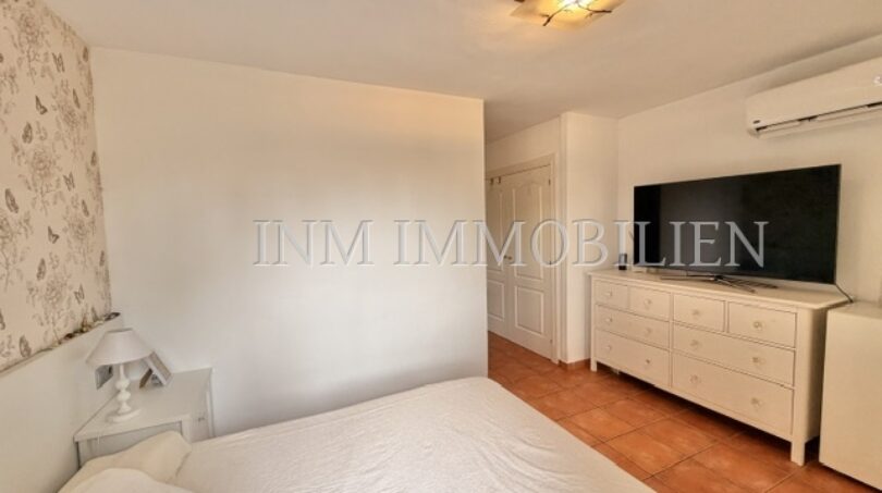 Helles Schlafzimmer mit Doppelbett, weißer Kommode, Flachbild-TV und Terrakottaboden im Reiheneckhaus Pollença