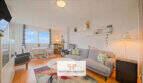 Helles Wohnzimmer mit grauem Sofa, bunten Kissen, Esstisch und Meerblick durch große Fenster in der 5. Etage