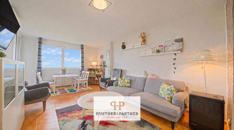 Helles Wohnzimmer mit grauem Sofa, bunten Kissen, Esstisch und Meerblick durch große Fenster in der 5. Etage