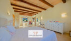 Amplio dormitorio de la finca Felanitx con techo de vigas de madera, cama doble y cómoda blanca
