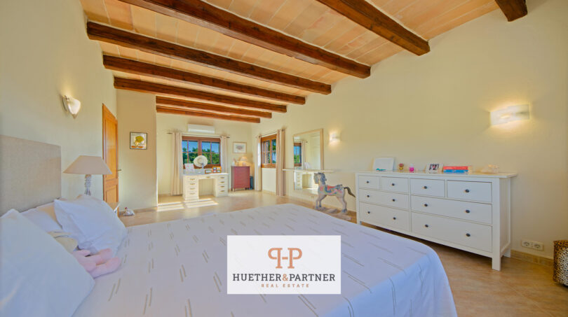 Amplio dormitorio de la finca Felanitx con techo de vigas de madera, cama doble y cómoda blanca