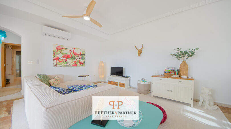 Helles Wohnzimmer mit Deckenventilator, Klimaanlage, Sofa, TV und tropischem Flamingo-Bild in Haus Cala Murada