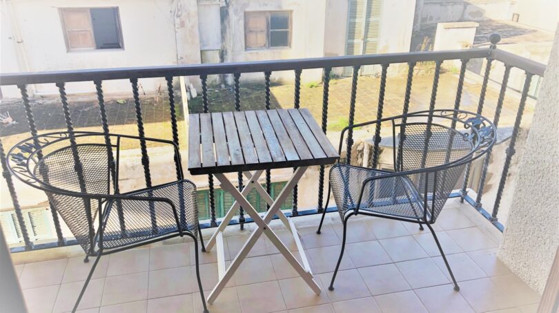 Balkon der Mietwohnung in Cala Ratjada mit zwei Eisenstühlen, Holztisch und Blick auf Nachbargebäude