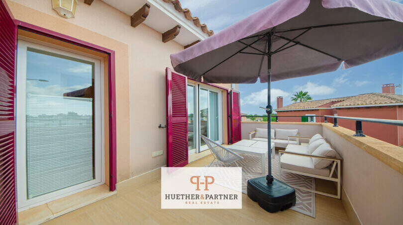 Sonnige Dachterrasse mit Sonnenschirm, weißen Loungermöbeln und pinken Fensterläden in Cala Murada