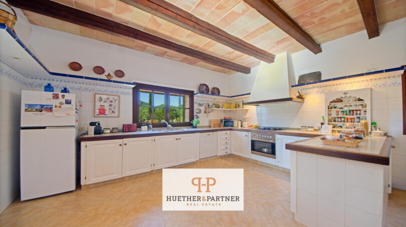 Geräumige Landhausküche der Finca Felanitx mit Holzbalkendecke, weißen Schränken und rustikalem Charme.