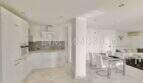 Offene Wohnküche mit weißen Einbauschränken, Glassesstisch und Marmorböden im Penthouse Cala Pi
