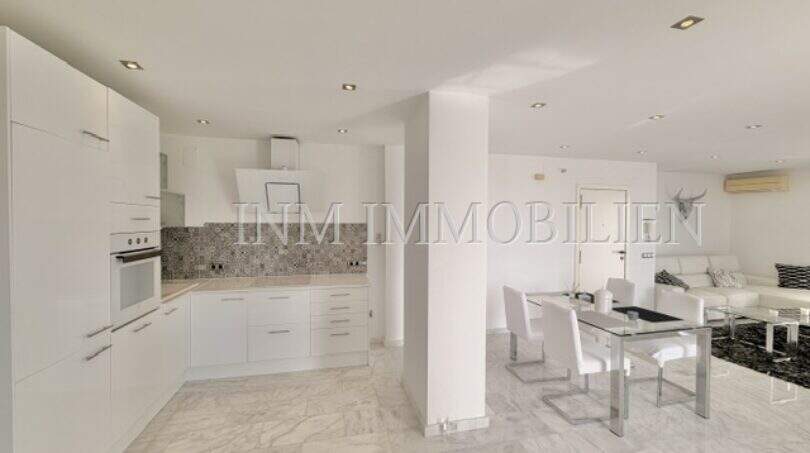 Offene Wohnküche mit weißen Einbauschränken, Glassesstisch und Marmorböden im Penthouse Cala Pi
