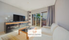 Helles Wohnzimmer der Mallorca-Wohnung mit Sofa, TV und Glasschiebetür zum sonnigen Balkon mit Palmenblick.