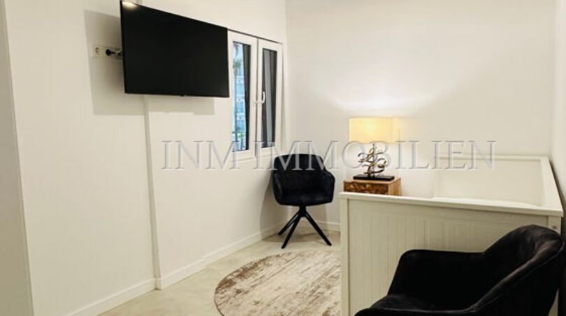 Modern living room of the designer apartment in Palma with black designer chairs, flat-screen TV and stylish ceiling lamp.