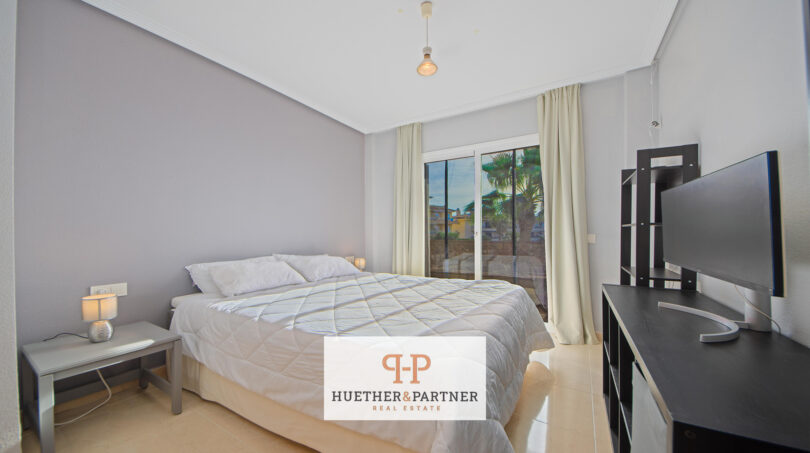 Helles Schlafzimmer der Mallorca-Wohnung mit Doppelbett, TV und Balkontür mit Palmenblick.