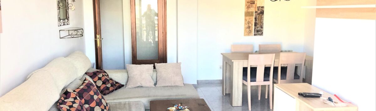Helles Wohnzimmer der Mietwohnung in Cala Ratjada mit Ecksofa, Couchtisch und Essbereich mit Holztisch.